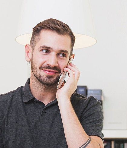 junger Mann mit Smartphone am Ohr telefoniert lächelnd in hellem Raum