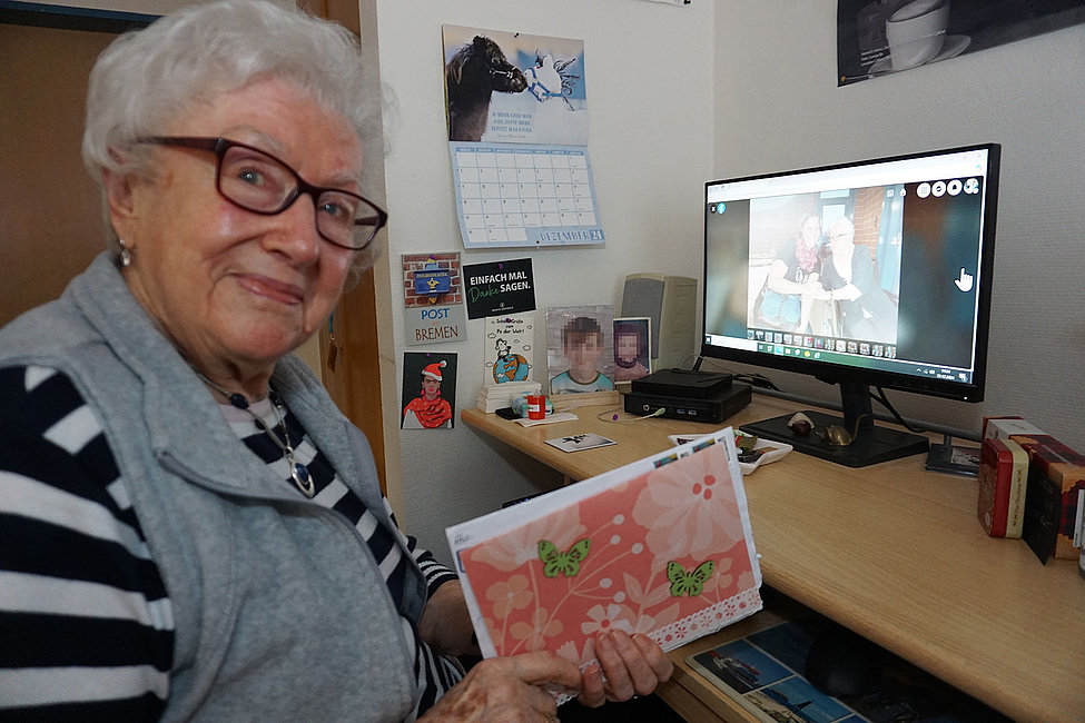 Ältere Frau hält Briefumschlag, Computer zeigt Videoanruf ihrer Brieffreundin