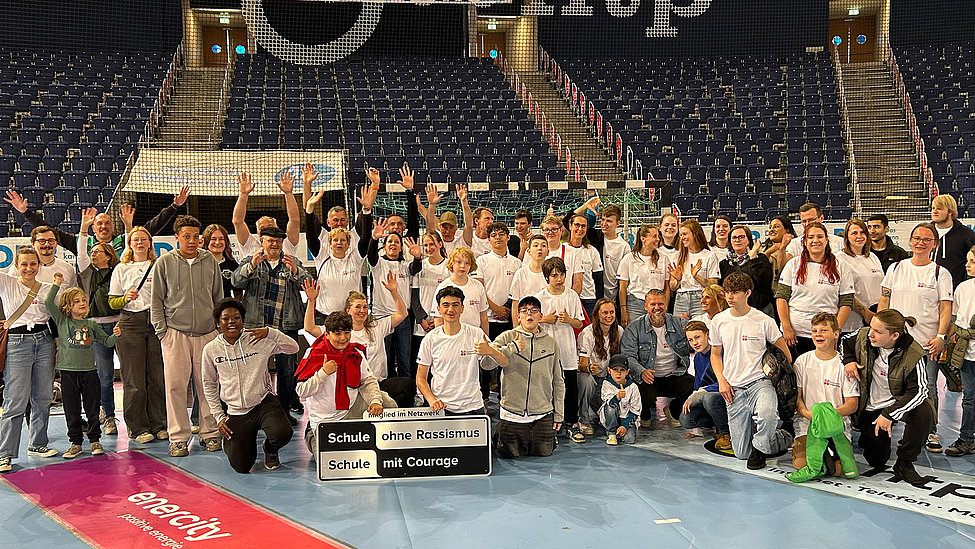 Schulgruppe in Arena mit Schild Schule ohne Rassismus – Schule mit Courage