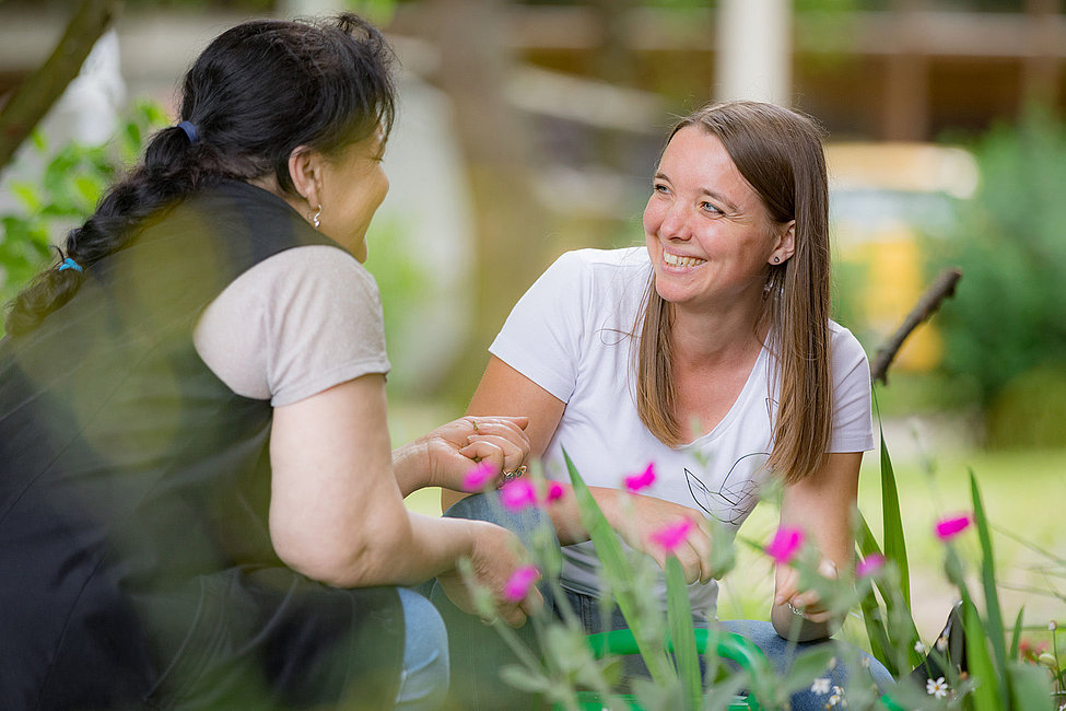 Zwei Frauen lächeln und halten Hände im Garten zwischen Blumen