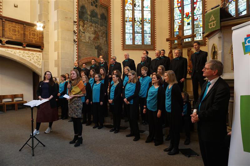 Chor im Stephansstift vor bunten Kirchenfenstern, Frau mit Mikrofon